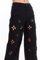 Model wears the Kaia Pearl High Rise Jean - Black, a straight-leg style with high waist, featuring large flower-shaped cutouts accented by silver studs that reveal skin beneath.