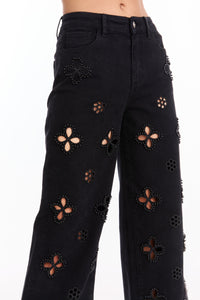 Model wears the Kaia Pearl High Rise Jean - Black, a straight-leg style with high waist, featuring large flower-shaped cutouts accented by silver studs that reveal skin beneath.